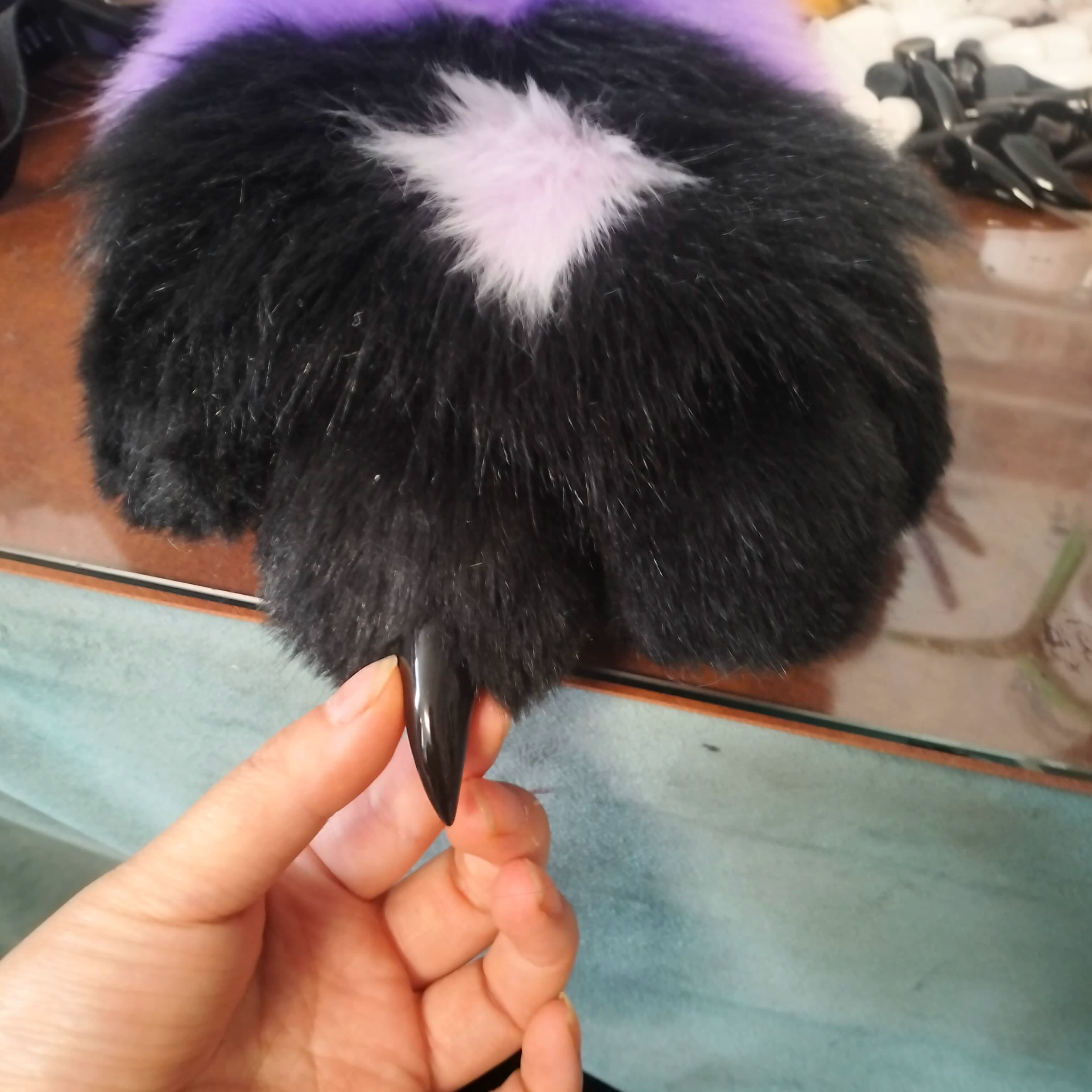 Black fursuit paw with purple accent fur and sharp resin claw closeup, held in artist's hand