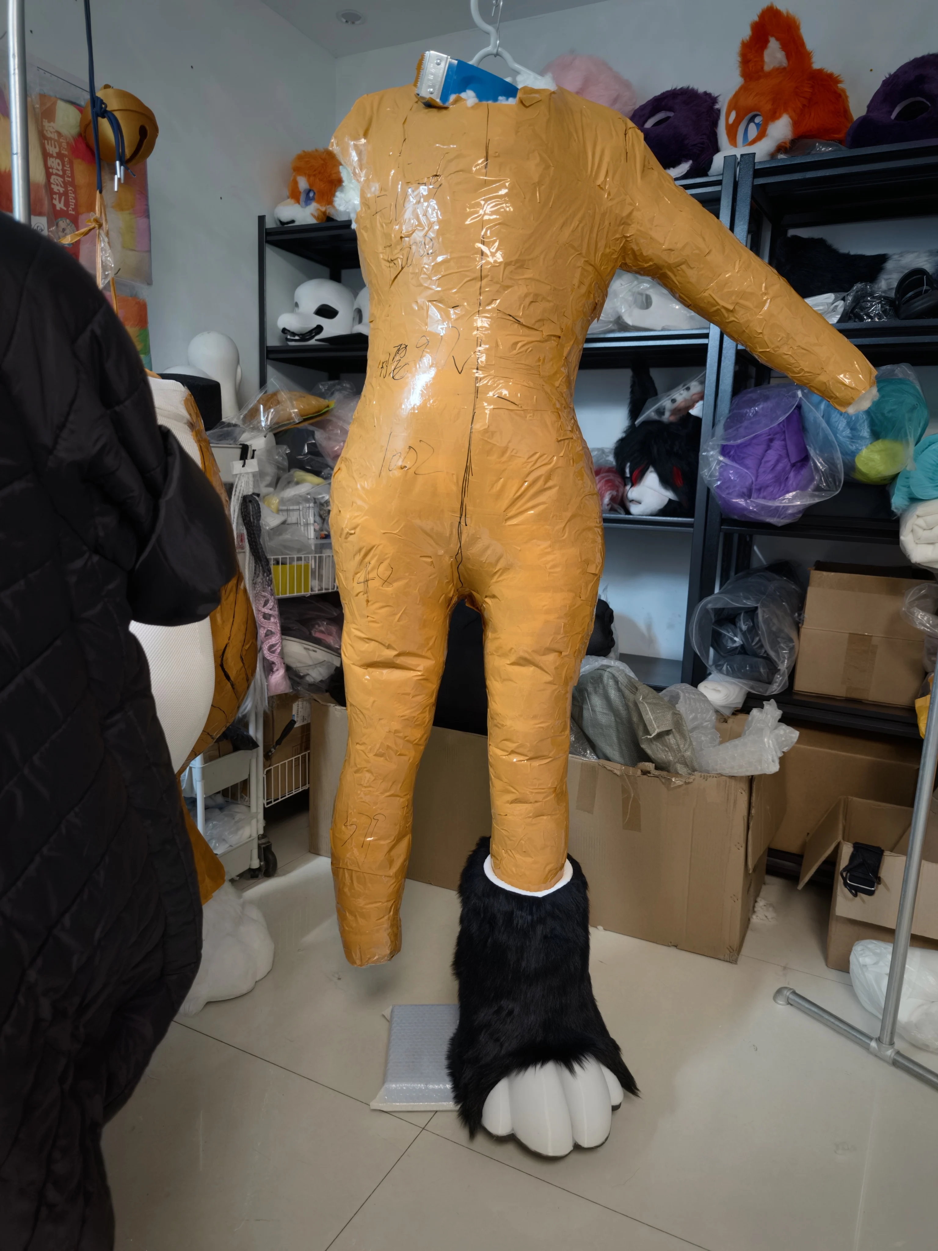 Behind the scenes fursuit bodysuit base in progress, foam and tape mannequin with black fur leg and paw attached in artist's workshop